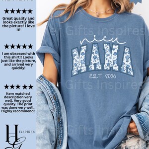 May include: A blue jean-colored t-shirt with the words "NICU MAMA" in white script and floral print lettering. The shirt also features "EST. 2026" in a simple font. The shirt is a comfortable, casual style.