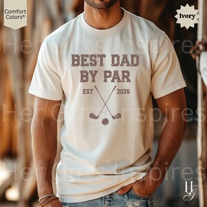 Peut inclure: T-shirt ivoire avec l'inscription "BEST DAD BY PAR" en police vieillie. Le motif comprend des clubs de golf crois&eacute;s et une balle, avec "EST 2026" imprim&eacute; en dessous. Le t-shirt est &agrave; manches courtes.