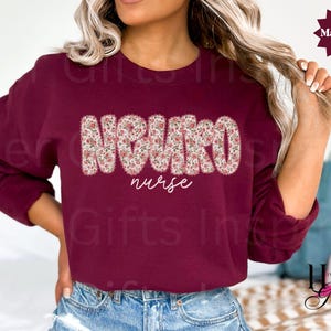 Puede incluir: Una sudadera burdeos con la palabra "NEURO" en un estampado floral en el pecho, con "nurse" escrito debajo en cursiva. La sudadera es de color burdeos liso.