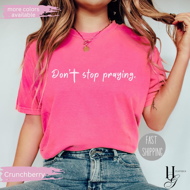 May include: A bright pink t-shirt with the text "Don't stop praying" in white script. The shirt is a crew neck style and is paired with blue jeans. The image also includes the text "more colors available" and "Fast Shipping".