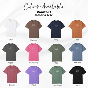 May include: A color chart displaying twelve Comfort Colors 1717 t-shirts in white, espresso, navy, yam, pepper, crunchberry, moss, blue jean, crimson, violet, light green, and black. Each shirt features small white text centered on the chest.
