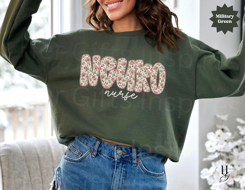 Puede incluir: Sudadera verde militar con la palabra "NURSE" en un estampado floral y la palabra "nurse" en escritura blanca. La sudadera es de manga larga y cuello redondo.