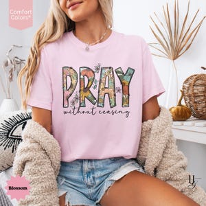 May include: A light pink t-shirt with the word "PRAY" in a floral design, and the words "without ceasing" underneath. The shirt is a Comfort Colors brand and the color is Blossom.
