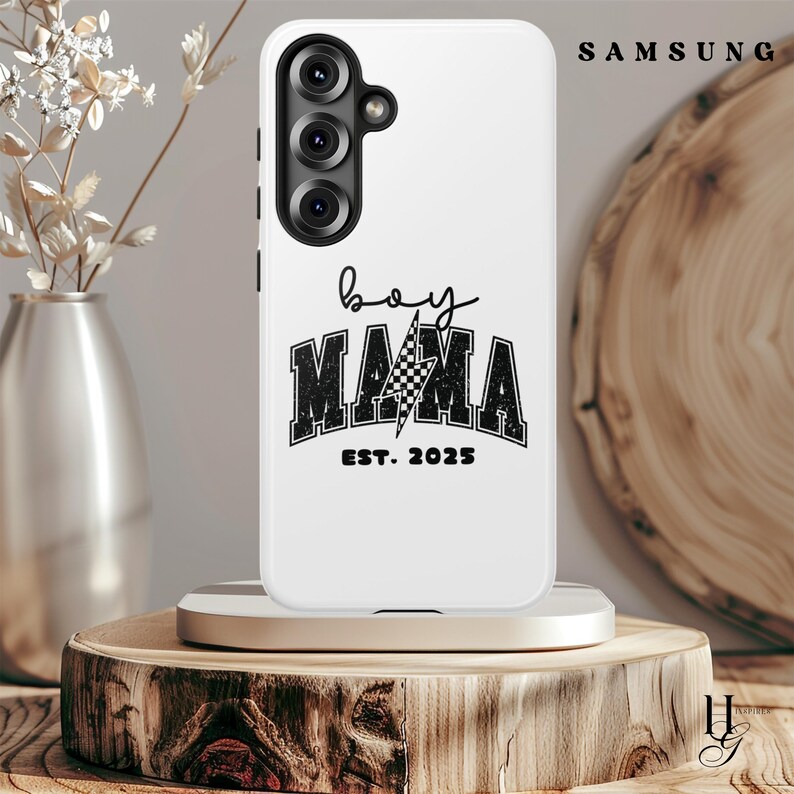Puede incluir: Carcasa blanca para tel&eacute;fono Samsung con un dise&ntilde;o de bandera de carreras a cuadros en blanco y negro y el texto "boy mama est. 2025".