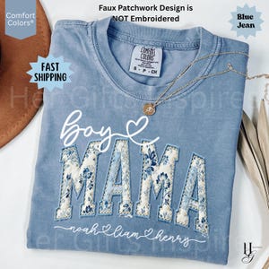 May include: A blue jean Comfort Colors t-shirt with "Boy Mama" in white script and floral patchwork letters. The names "Noah, Liam, Henry" are below. A gold necklace is draped across the shirt. The text "Faux Patchwork Design is NOT Embroidered" is at the top.