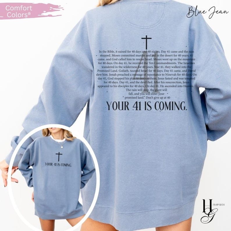 May include: A blue jean colored crewneck sweatshirt featuring a black cross graphic and text on the back detailing biblical events related to the number 40, with the phrase "YOUR 41 IS COMING." A smaller version of the graphic is on the front chest.