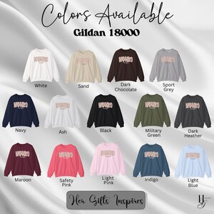 Puede incluir: Una selecci&oacute;n de sudaderas Gildan 18000 en varios colores, incluyendo blanco, arena, chocolate oscuro, gris deportivo, azul marino, ceniza, negro, verde militar, gris oscuro, granate, rosa de seguridad, rosa claro, &iacute;ndigo y azul claro. Cada sudadera presenta la palabra "NOUKO" en un dise&ntilde;o floral.