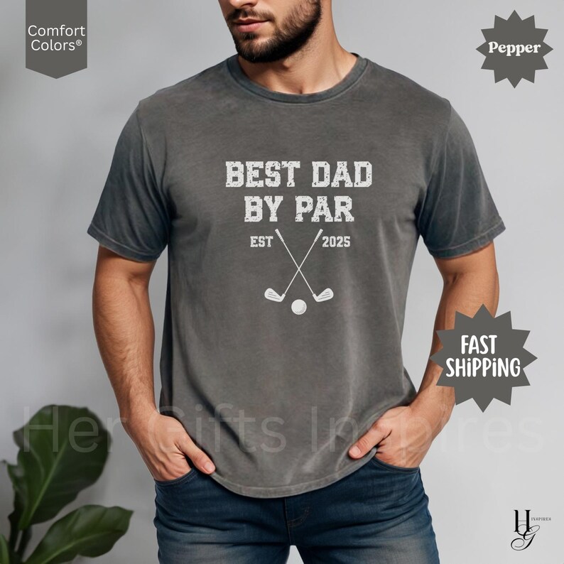 Peut inclure: Un t-shirt gris avec l'inscription blanche "BEST DAD BY PAR", des clubs de golf crois&eacute;s et une balle de golf. Le t-shirt affiche &eacute;galement "EST 2025". Le t-shirt est de la marque Comfort Colors.