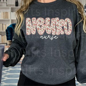 Puede incluir: Sudadera gris oscuro con la palabra "NURSE" en un dise&ntilde;o floral en el pecho. Debajo, la palabra "nurse" est&aacute; escrita en cursiva. Un vaso plateado con pajita se sostiene en la mano izquierda.