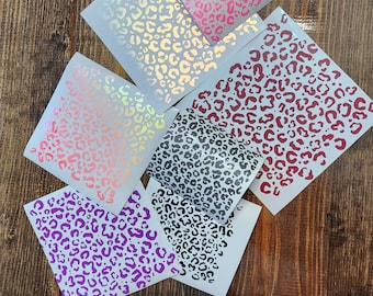 May include: Six sheets of vinyl with leopard print designs in various colors, including pink, red, gray, and purple. The sheets are on a wooden surface.