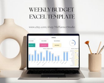 May include: A laptop computer displaying a weekly budget excel template with a green total income box, a pink total expense box, and a blue total difference box. The screen also shows a pie chart and bar graphs. The laptop is on a white desk with a beige vase and paintbrushes.