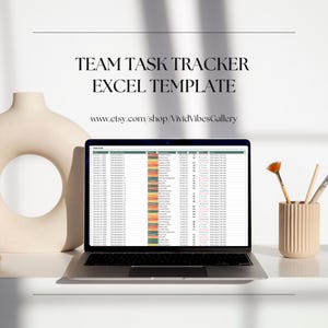 May include: A laptop computer displaying a spreadsheet with the title "Team Task Tracker Excel Template". The spreadsheet is filled with data and color-coded cells. The laptop is on a white surface with a vase of paintbrushes.