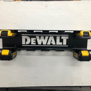 May include: Black metal wall mount with the word "DEWALT" in white lettering. The mount has slots for holding four yellow and black power tool batteries.