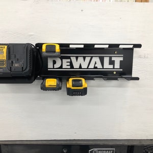 May include: Black metal wall mount with the word "DEWALT" in white lettering. The mount has slots for holding four batteries and a charger. There is a yellow and black DEWALT battery charger and three yellow and black DEWALT batteries on the mount.
