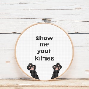 May include: A white embroidery hoop with black text that reads "show me your kitties" and two black cat paws with pink paw pads.