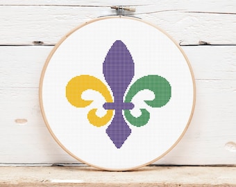 May include: A purple, green, and yellow fleur-de-lis cross stitch pattern on white fabric in a wooden embroidery hoop.