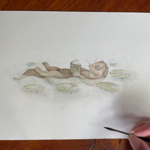 Lontra che fluttua tra le ninfee mentre legge un libro, stampa artistica ad acquerello, stampa di lontra dipinta a mano, stampa di lontra per bambini, arte murale di lontra