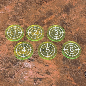 May include: Six transparent yellow game tokens with white target designs and numbers 1 through 6. The tokens are arranged in a semi-circle on a brown surface. Dice are visible in the lower right corner.