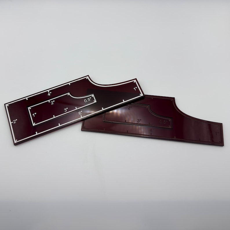 May include: Two burgundy acrylic quilting rulers with white markings. One ruler has a rectangular shape with a cutout and measurements in inches. The other ruler is a smaller, curved shape with inch markings. Ideal for quilting projects.