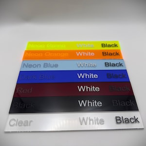 May include: A stack of acrylic color samples in neon green, neon orange, neon blue, dark blue, red, black, and clear. Each sample has the word "White" and "Black" printed on it.