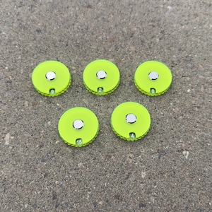 以下が含まれることがあります： 銀色の中心と縁に数字が付いた、5つのネオングリーンの円形オブジェクト。数字は0、2、4、9、15です。オブジェクトは、グレーのテクスチャのある表面にあります。