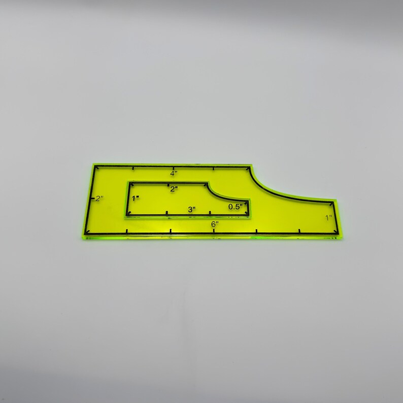 May include: A neon yellow quilting ruler with black markings. The ruler has various measurements in inches, including 1", 2", 3", 4", 6", and 0.5". The ruler is designed with a unique shape for quilting projects.
