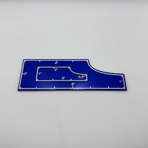 May include: A blue quilting ruler with white markings and measurements in inches. The ruler has a unique shape with a curved edge and a cutout. Measurements include 6", 4", 3", 2", 1", 0.5", and -2".
