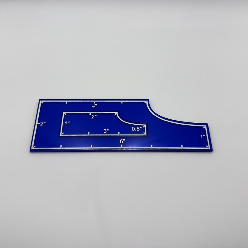 May include: A blue quilting ruler with white markings and measurements in inches. The ruler has a unique shape with a curved edge and a cutout. Measurements include 6", 4", 3", 2", 1", 0.5", and -2".