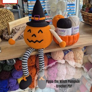 May include: A crocheted pumpkin figure with a witch hat, arms, and legs. The pumpkin is orange with a black witch hat and a purple buckle. The legs are black and white striped. The text "Pippa the Witch Pumpkin - Crochet PDF" is visible.