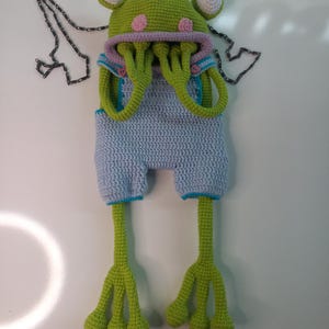 Peut inclure: Ensemble fait main au crochet, comprenant un chapeau et un short d'extraterrestre, vert, bleu, rose et blanc. Le chapeau a de grands yeux et des taches roses, avec de longues tentacules vertes. Le short bleu a une bordure turquoise.