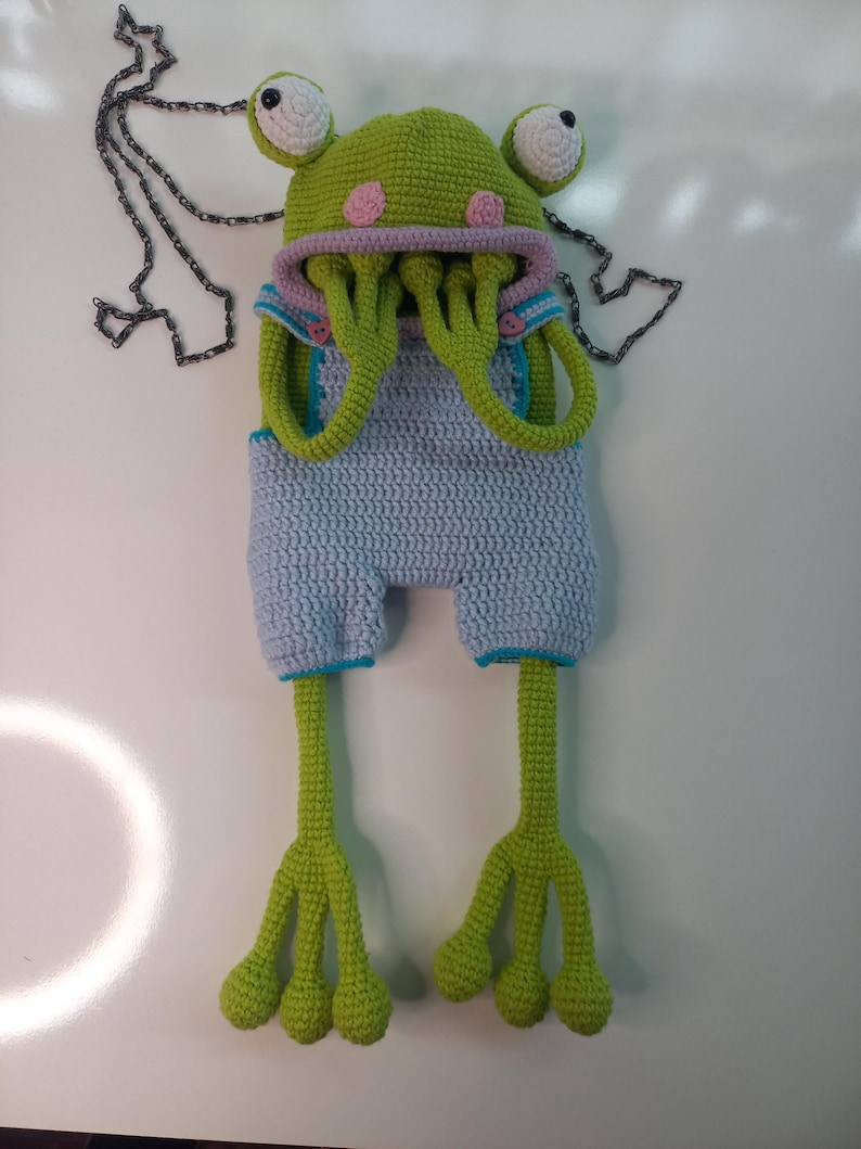 Peut inclure: Ensemble fait main au crochet, comprenant un chapeau et un short d'extraterrestre, vert, bleu, rose et blanc. Le chapeau a de grands yeux et des taches roses, avec de longues tentacules vertes. Le short bleu a une bordure turquoise.