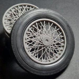 Puede incluir: Dos ruedas de radios grises con neumáticos negros. Las ruedas tienen un diseño clásico y vintage con numerosos radios que irradian desde el buje central. Los neumáticos son negros y tienen un dibujo detallado de la banda de rodadura. Las ruedas son probablemente para un coche de modelo o un vehículo vintage.