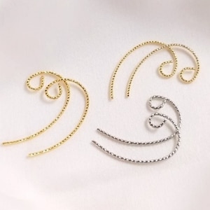 May include: Two pairs of gold and silver ear cuffs. The ear cuffs are made of twisted wire and have a curved shape.