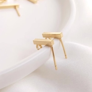 May include: Two gold bar earrings with a post and butterfly backing. The earrings are on a white surface.