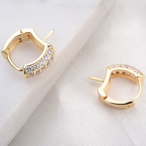 May include: A pair of gold hoop earrings with a row of clear cubic zirconia stones around the hoop.