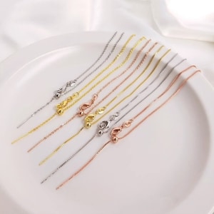 May include: Assortment of delicate chain extenders in gold, silver, and rose gold finishes. Each extender features a small ball at the end and a lobster clasp.