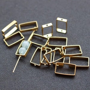 Op de afbeelding: Een groep gouden metalen rechthoekige frames met kleine gaten. Sommige frames hebben een kraal erin.