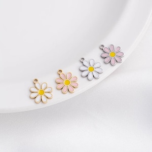 May include: Four metal daisy charms with yellow centers. The daisies are in white, pink, and gold.