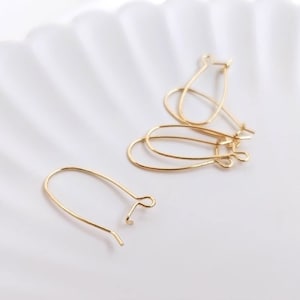 May include: A set of four gold-toned metal earring hooks, each featuring a U-shaped wire design with a small loop at the end for attachment. The components are arranged in a loose cluster, showcasing the smooth, polished finish of the metal wire.