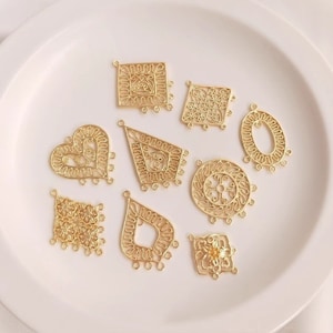 May include: A set of nine gold filigree metal charms with intricate designs. The charms include a heart, a square, a circle, a diamond, and several other shapes. Each charm has three jump rings for attaching to jewelry or other crafts.