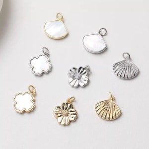 Pode incluir: Conjunto de pingentes de metal em tom prateado e dourado, incluindo uma flor, uma concha e um trevo. Os pingentes são perfeitos para fazer joias ou para adicionar um toque de fantasia às suas manualidades.