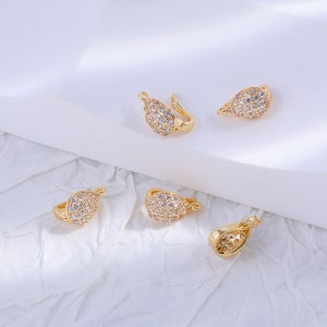 May include: Five gold-toned jewellery clasps with clear crystal accents. The clasps are shaped like teardrops and have a loop on one end for attaching to a necklace or bracelet.