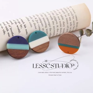 以下が含まれることがあります： 青、緑、白、オレンジの層状のデザインが施された、丸い木とレジン製のイヤリングが3つ。イヤリングの上部に吊り下げ用の穴があります。