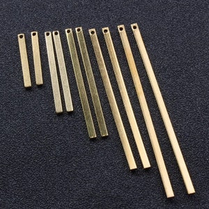 Peut inclure: Un ensemble de 12 pendentifs en barre de métal doré, chacun d'une longueur différente, allant d'environ 2,5 cm à 10 cm. Les barres sont lisses et ont une finition polie.