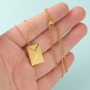 Könnte beinhalten: Eine goldfarbene Halskette mit einem kleinen Anhänger in Form eines Briefumschlags. Die Kette ist in einem zarten, verlinkten Stil.