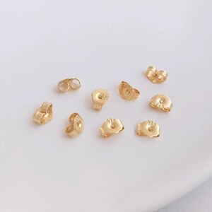 May include: A collection of gold-toned earring backs. The backs are made of metal and have a variety of shapes and sizes. Some of the backs have the number "925" stamped on them.