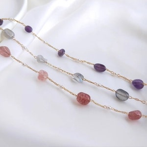 Op de afbeelding: Een gouden ketting met drie strengen van verschillende gekleurde stenen. De stenen zijn amethyst, labradoriet en rozenkwarts.