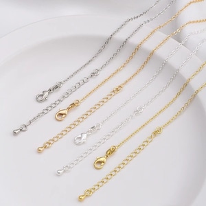 Könnte beinhalten: Fünf silberne und goldene Kettenverlängerungen mit Karabinerhaken und Kugelenden.