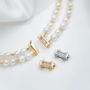 May include: Close-up of a double-strand pearl necklace with gold accents and a rectangular clasp with clear crystals. Two additional clasps, one gold and one silver, are also visible.
