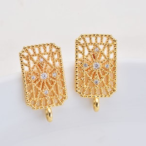 May include: A pair of gold-tone earrings with a geometric design and clear crystal accents. The earrings have a rectangular shape with a delicate, openwork pattern.